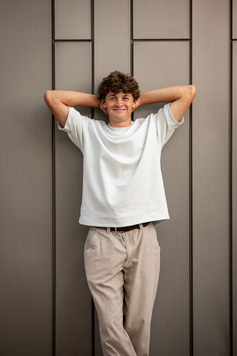 A boy relaxes with arms above his head in urban scene.