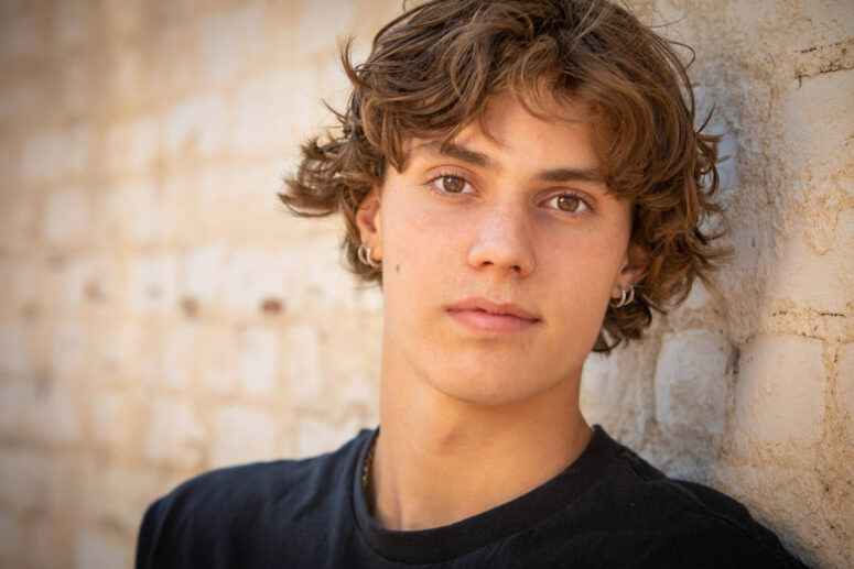 A high school senior stands against white brick wall in Fort Collins.