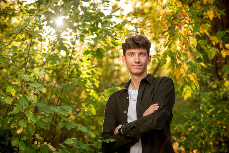 A student smiles in green leaves as sun comes through.