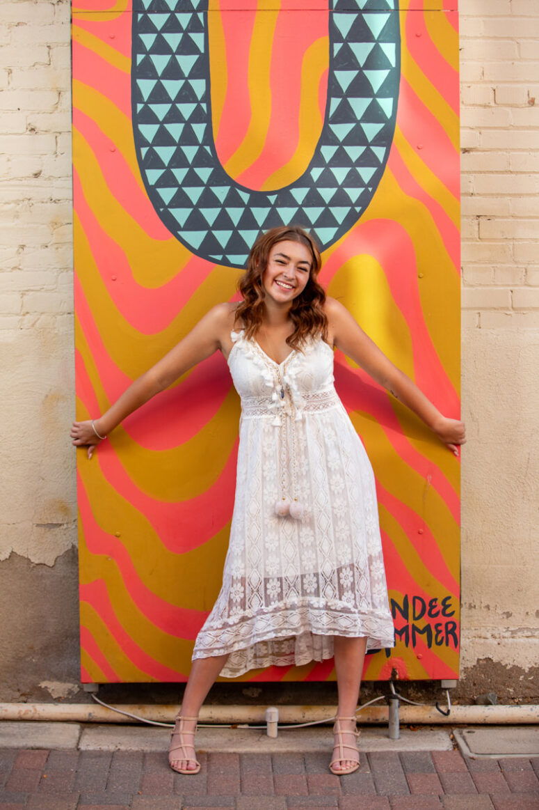 Laughing high school senior against colorful mural in Fort Collins.