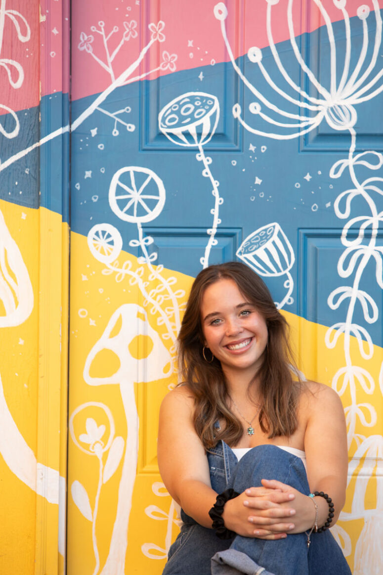 Girl smiling against colorfully painted door.