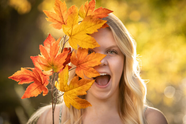 A girl smiles with a fall leaf in front of her face.