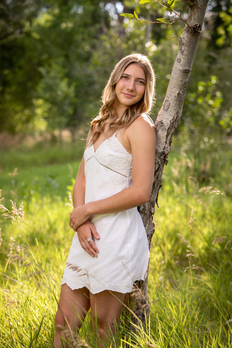 Student in white dress in green field with trees.