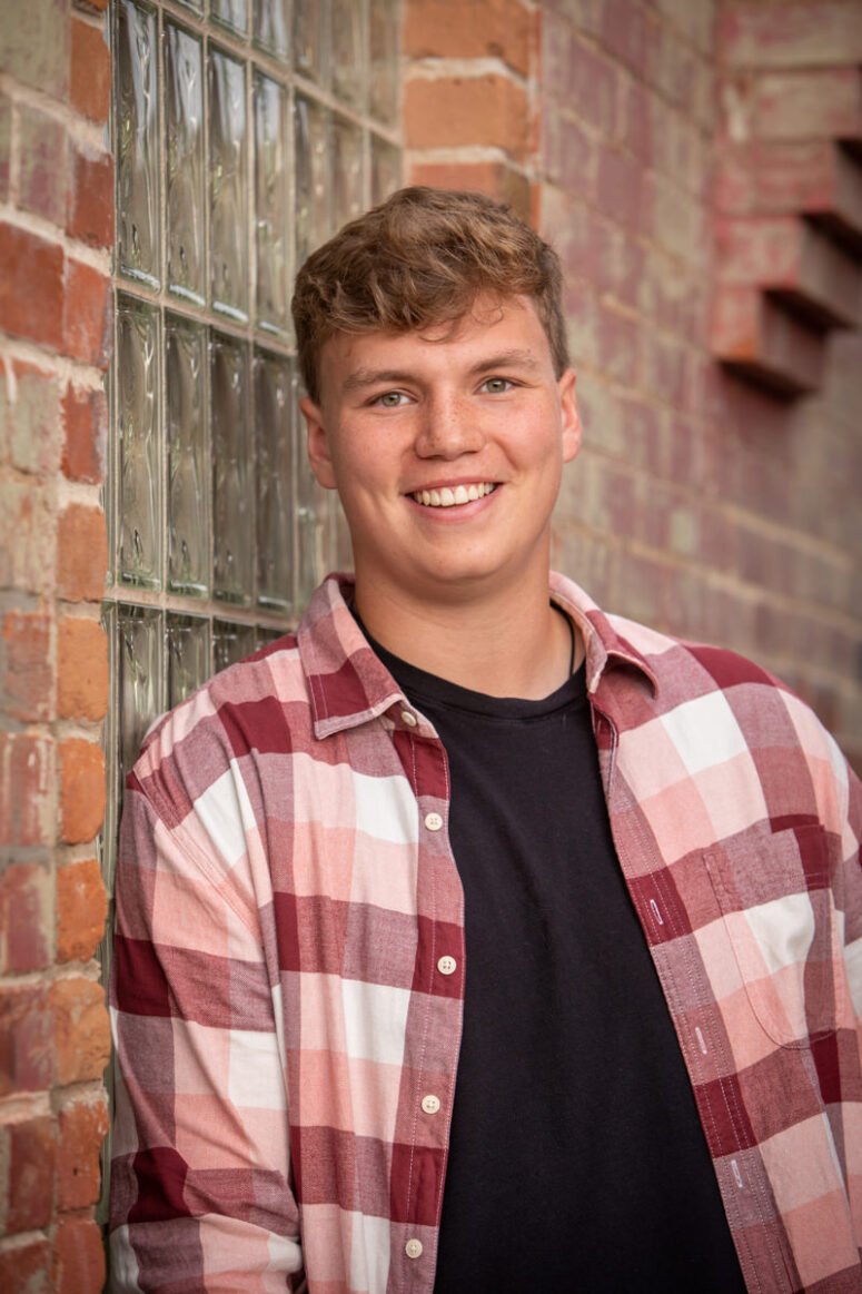 A boy smiles in a plaid shirt.