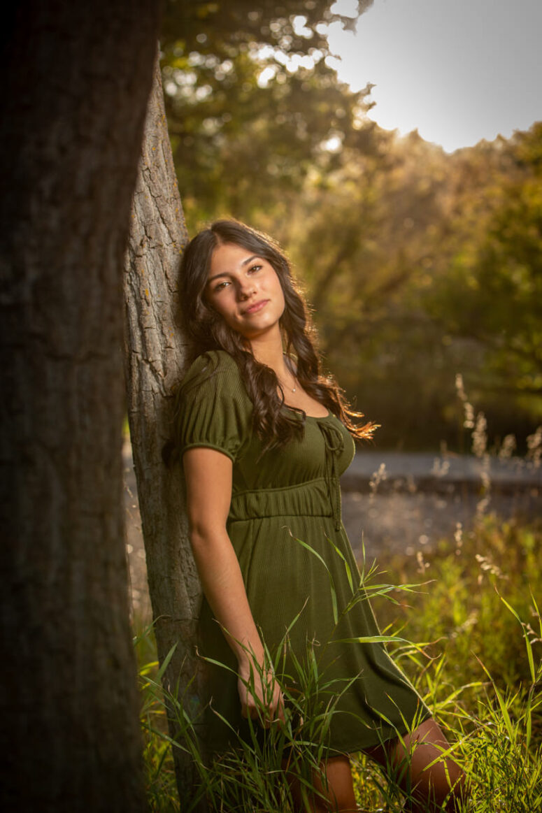 A girl in a green dress resting against a tree.